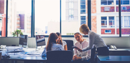 A group of business women conversing in a formal office setting. 