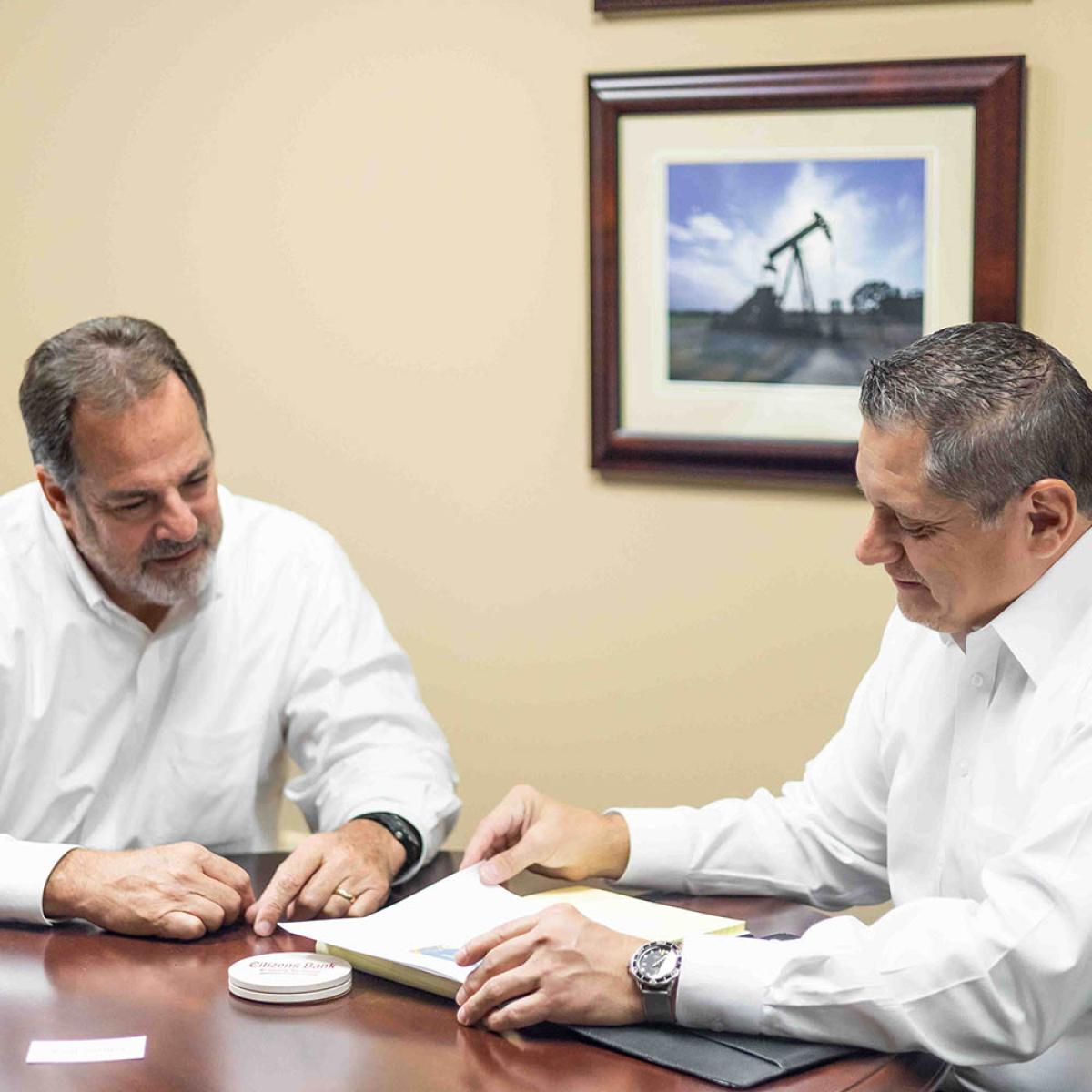 two men sitting at a table looking at papers