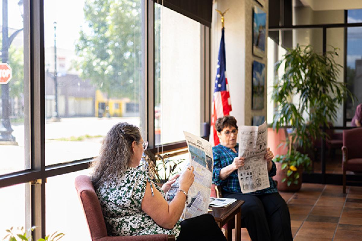 Two women sitting reading newspapers by a window