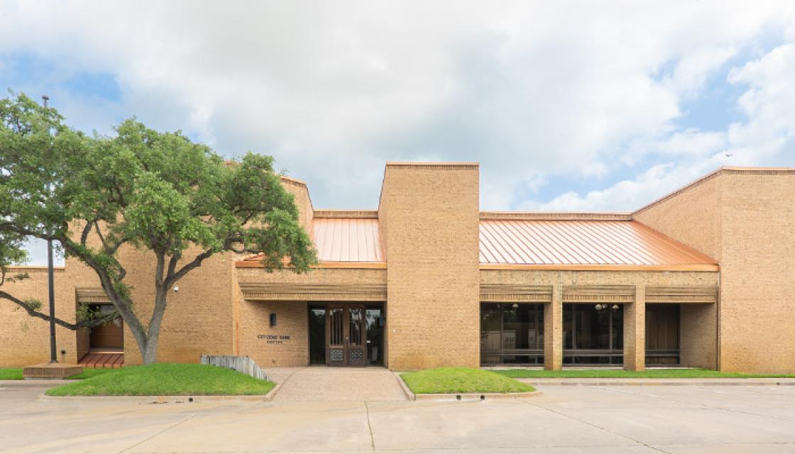 entrance to large tan brick building with oak tree in front